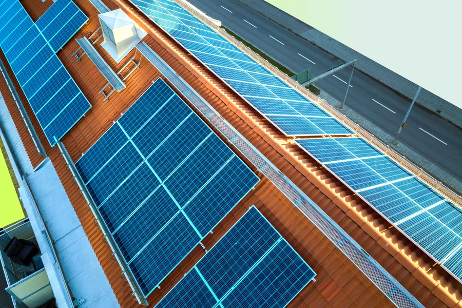 Luftaufnahme eines Mehrparteienhauses mit Photovoltaik auf dem Dach, Nachbargrundstücke in den Lumitra-Markenfarben abgedeckt