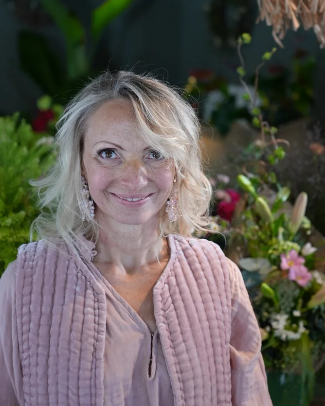 Frau in rosa Leinenjacke vor Blumen und Pflanzen im Laden
