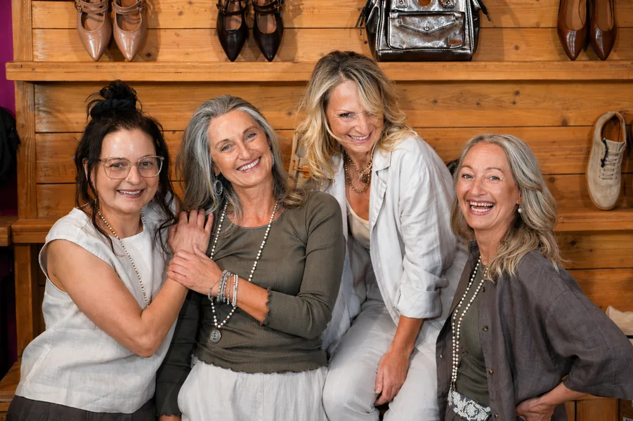 Vier Frauen lachen vor der Holzwand mit Schuhen und Taschen