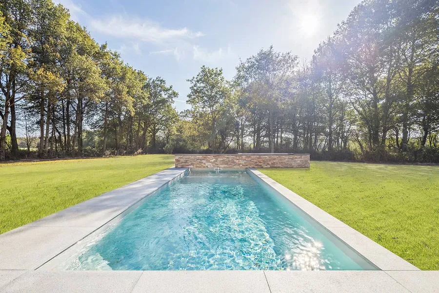 Langer Pool im Rasen mit Natursteinmauer und Bäumen