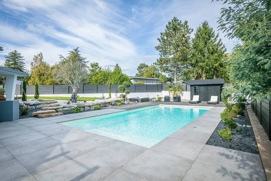 Pool-Anlage mit großer Betonterrasse, Steinmauer und Bepflanzung